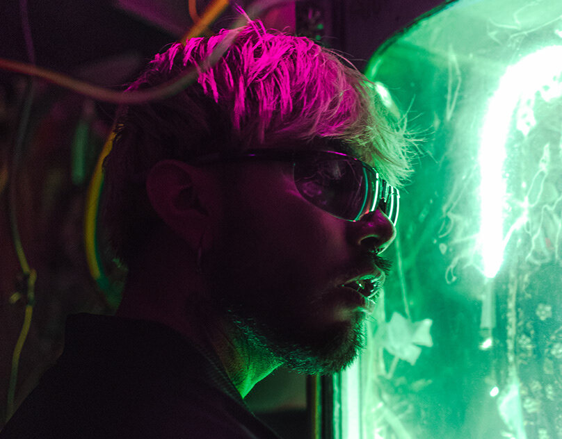A figure lit in magenta and green neon — moody nightlife portrait.