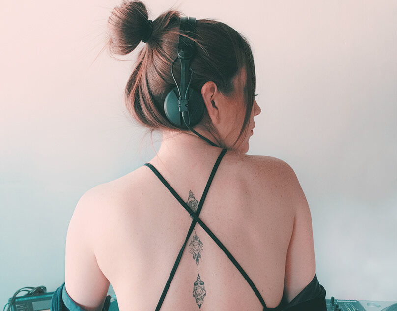A bare-shouldered figure seen from behind wearing headphones — urban-soft portrait.