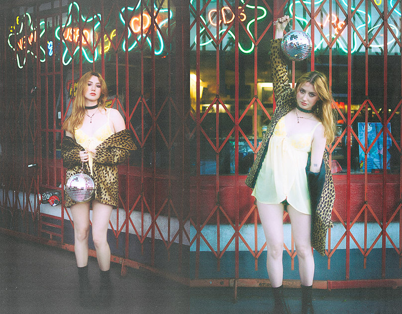 Two figures dressed in white against a colorful stained-glass backdrop.
